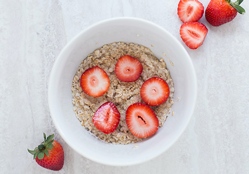 A bowl of healthy breakfast oatmeal with strawberry slices is pictured from above.