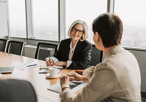 Two businesswomen discussing insurance lead follow-up strategies during a meeting in a modern office.