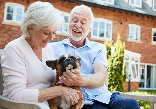 Retired Couple Sitting On Bench With Pet French Bulldog In Assisted Living Facility